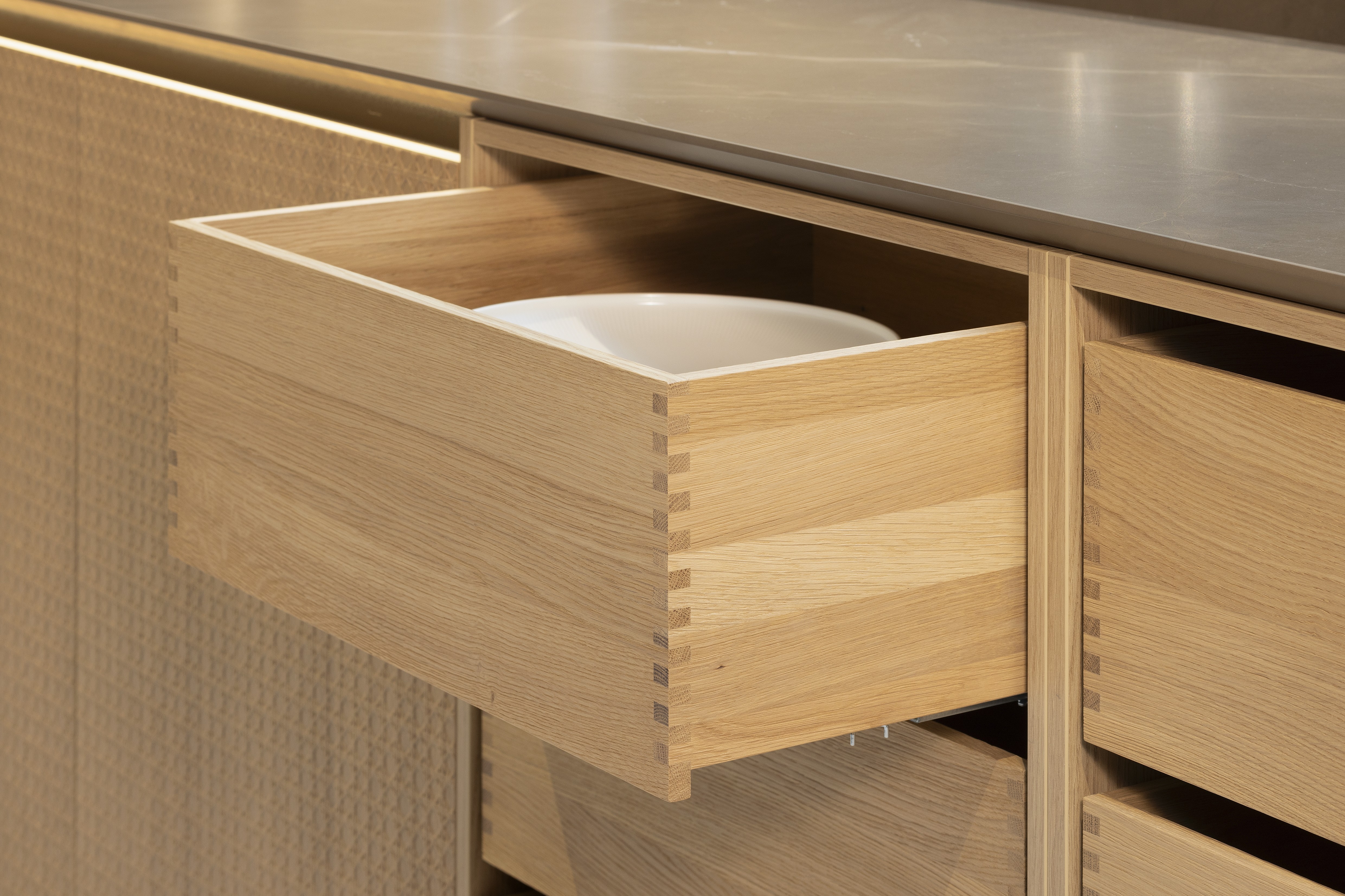 APL: Pulpis (Keramik) 25 mm Front: AV 6085-GL Eiche-elegant Echtholzfurnier (PURemission) Korpus: 2085 Designkorpus Feineiche-natur Griff: Kehlleiste 355 Schwarz matt Geräte: Siemens  Armatur: Gessi Spüle: ?  Features: neue Oberfläche Wiener Geflecht in Echtholzfurnier, Oberflächenmix, Waschbecken (Spülstein) in APL-Material, schwebende Arbeitsplatte durch Lichtleiste, APL abgekantet (schwebend), Backöfen in Wand eingekoffert, 3 Materialfarben.