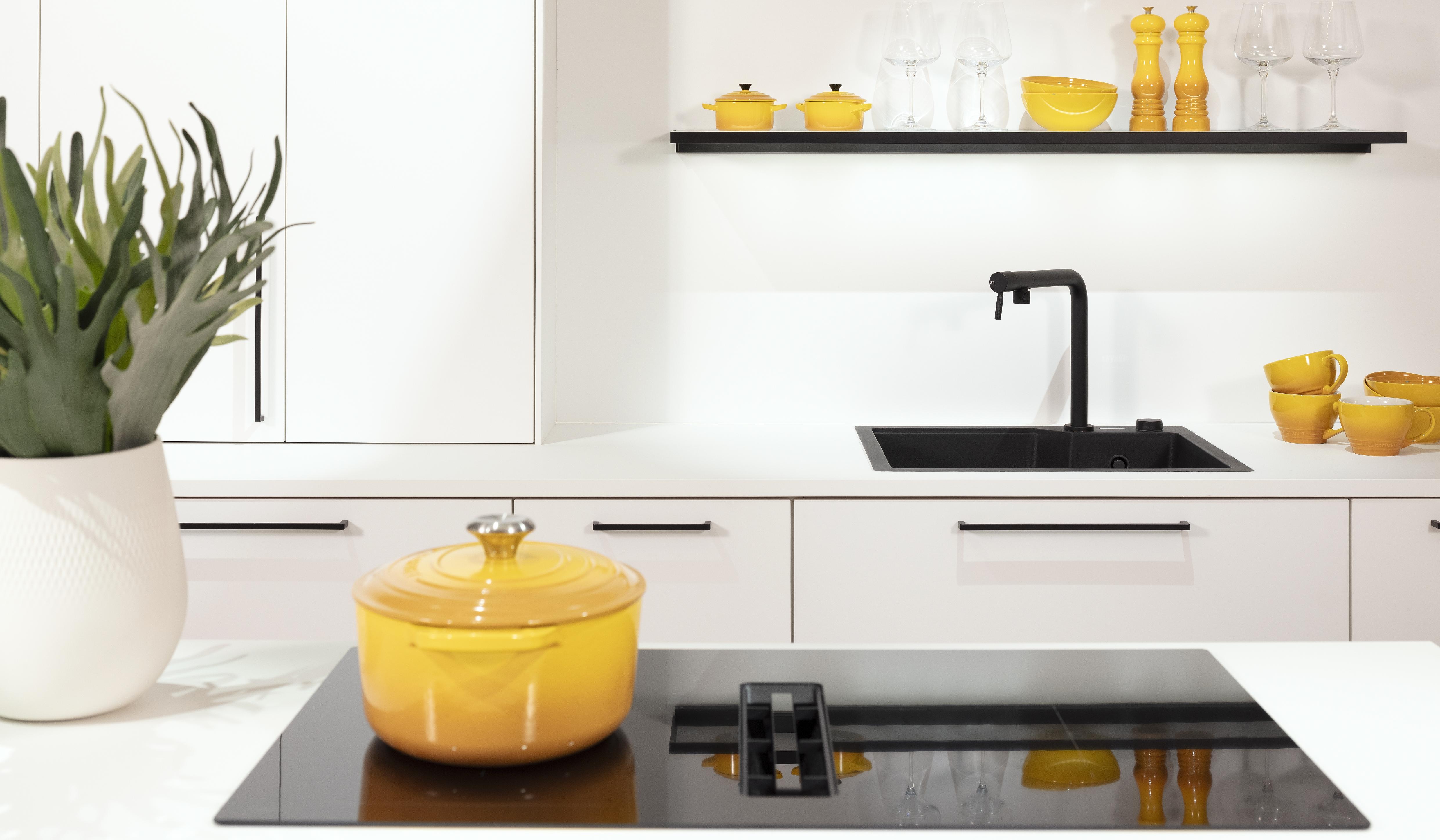 Kristallweiße Häcker-Küche mit Kochfeld auf Kücheninsel und Küchenzeile im Hintergrund