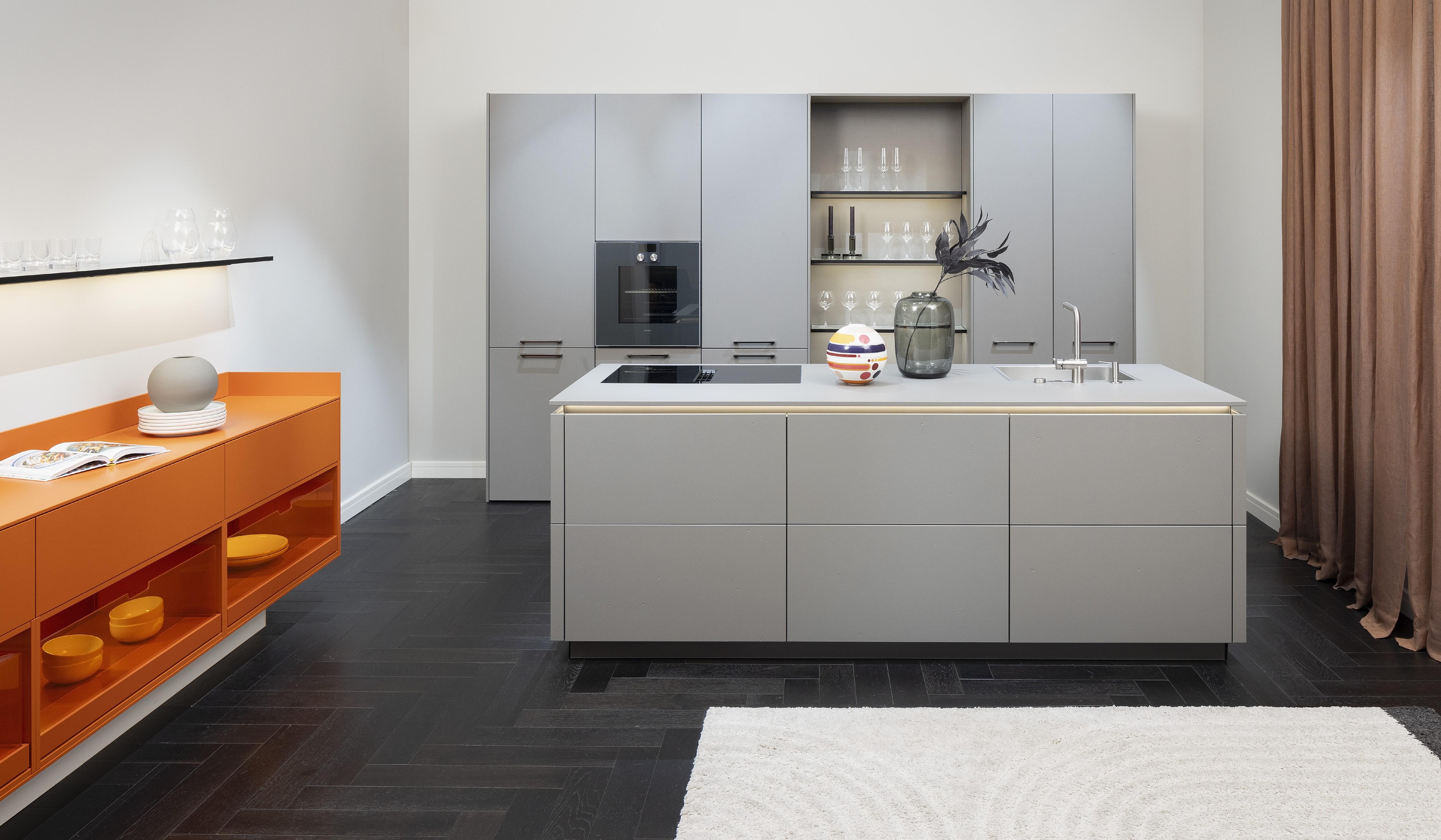 APL: 171 Greige 16 mm Front: AV 7010-GL Beton-grau, mineralischer Spachtelbeton (PUResist, PURemmision) Front Lack Orange Korpus: 2059 Designkorpus Titan Griff: Metall Black Chrome und Kehlleiste 359 Greige matt Kehlleiste Graphit gebürstet Geräte: Gaggenau Armatur: Franke Spüle: Franke  Features: Betonoberfläche individuell nachbearbeitet, Nischenrückwand Regal Betonoberfläche, Sideboard Orange mit offenen Schubkästen in Plexiglas Orange exklusives Auszugssystem im Schrank für mehr Stauraum, Sideboard 